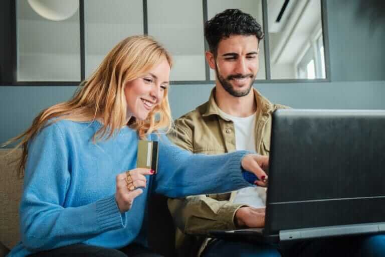Couple using a laptop to make an online purchase with a credit card, smiling while shopping together